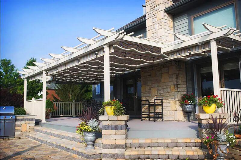 A pergola attached to a house with an awning made with unbrella fabric